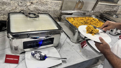 Guest serving yellow rice from a buffet warmer next to a pan of steamed rice